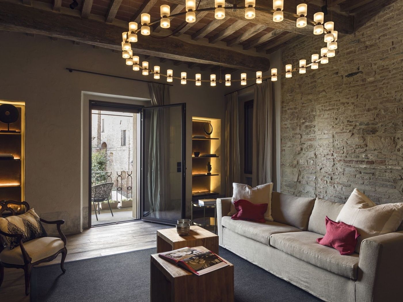 Salotto del Rastrello con soffitto a travi, parete in pietra e lampadario circolare